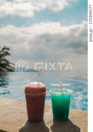 Two colorful cold drinks on pool edge with ocean horizon and soft cloudy sky creating tropical vacation refreshment scene with wide copy space for travel and resort concepts 135849577