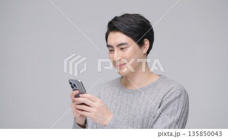 スマホを操作する30代男性 グレーバック スマホを操作する30代男性 グレーバック 135850043