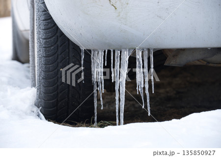 Close-up of icicles hanging from a car bumper in the winter snow 135850927