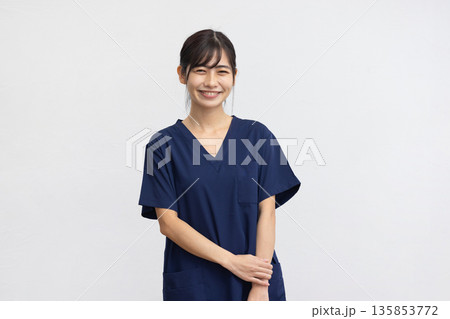 白背景の前で紺色の医療用スクラブを着て微笑む若い女性 白背景の前で紺色の医療用スクラブを着て微笑む若い女性 135853772