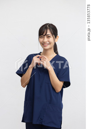 白背景の前で紺色の医療用スクラブを着て微笑む若い女性 135853778