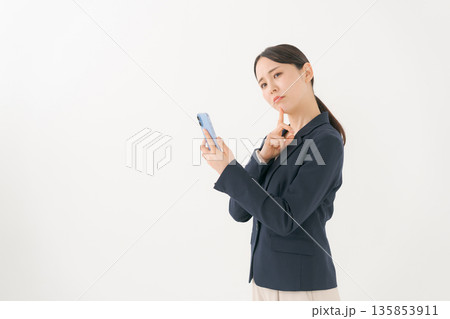 スマホを見て悩むスーツの女性 135853911