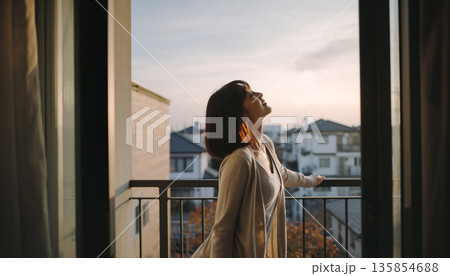 1. 朝のベランダで伸びをして微笑む20代女性 爽やかな目覚めとライフスタイル 135854688