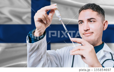 Doctor holding syringe on Finland flag background. Medical professional holding syringe with Finnish flag in the background Doctor holding syringe on Finland flag background. Medical professional holding syringe with Finnish flag in the background 135854697