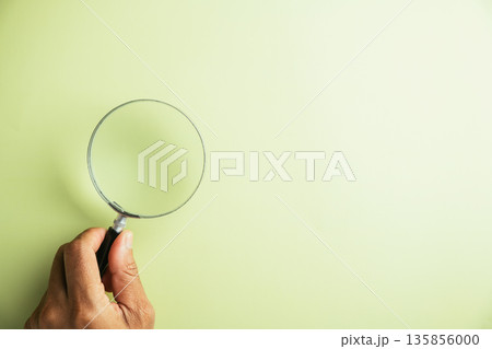 Hand holding a magnifying glass on a light green background. Perfect for search, investigation, or discovery concepts. 135856000