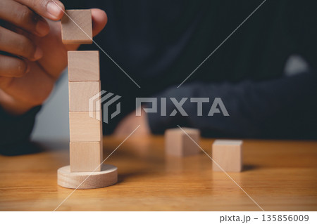 Hand placing wooden block on top of a tower, creating a concept of growth and success. 135856009
