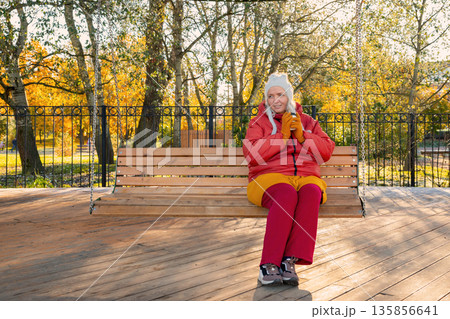 body positive Caucasian woman with a disposable cup of coffee dreams and sits on a wooden swing in an autumn park in the morning. Mental health, harmony with oneself, wellness body positive Caucasian woman with a disposable cup of coffee dreams and sits on a wooden swing in an autumn park in the morning. Mental health, harmony with oneself, wellness 135856641