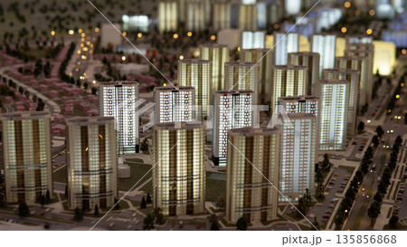 A model shows a city district with many buildings lit up at night. The layout includes streets, a park, and various real estate options, showcasing urban development. A model shows a city district with many buildings lit up at night. The layout includes streets, a park, and various real estate options, showcasing urban development. 135856868