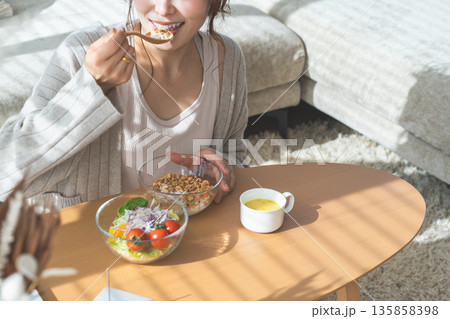 リビングテーブルに座りグラノーラ,サラダを食べる食事中の女性 135858398