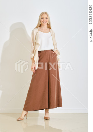 Elegant woman wearing a stylish outfit with wide brown pants in a bright indoor setting 135858426