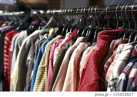 Colorful variety of vintage apparel and second-hand clothes hanging on a rack in a thrift shop or flea market. This image captures the concept of sustainable fashion, retro style, and the treasure 135858827