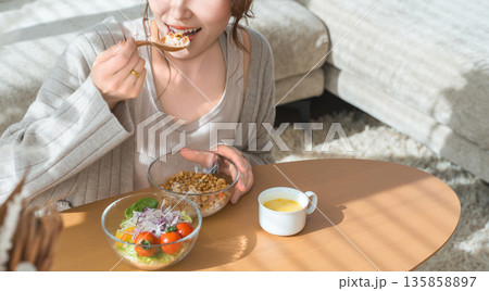 リビングテーブルに座りグラノーラ,サラダを食べる食事中の女性 135858897