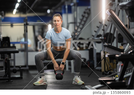 Woman exercising with kettlebell doing squats in gym 135860093