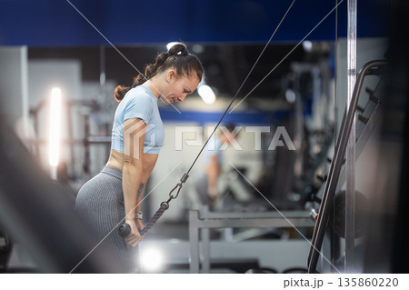 Woman training triceps using cable machine in gym 135860220