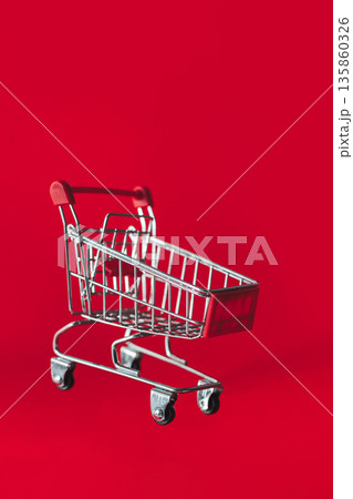 A miniature shopping cart floats against a bold red background A miniature shopping cart floats against a bold red background 135860326