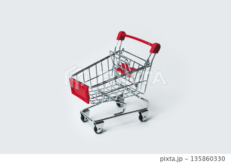 A miniature shopping cart rests on a clean white surface, side view A miniature shopping cart rests on a clean white surface, side view 135860330