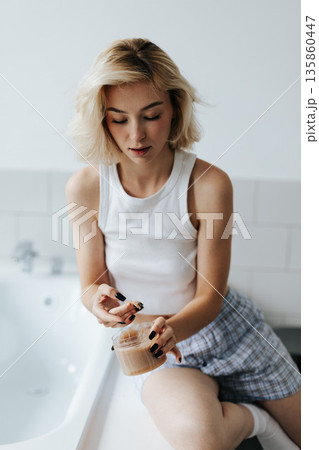 Woman Get Cosmetic Body Scrub From Jar Sitting On Bath In Bathroom Woman Get Cosmetic Body Scrub From Jar Sitting On Bath In Bathroom 135860447