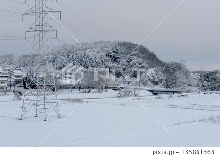 雪に覆われた郊外の街並みと送電鉄塔 冬の日本のインフラ風景 135861363
