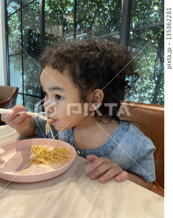 Cute little girl eating spaghetti with spoon in the kitchen in a restaurant. Healthy eating concept. 135862281
