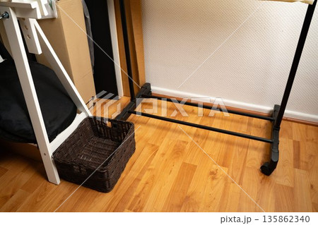 Brown woven basket placed next to wooden trestles and a shoe rack in a casual home interior. Simple storage and organization. Concept of home, interior, lifestyle, domestic, minimal. 135862340