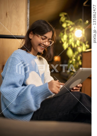 Smiling woman using tablet while working in cozy modern office lounge. Smiling woman using tablet while working in cozy modern office lounge. 135862477