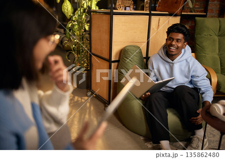 Young man using laptop during casual team discussion in modern office lounge. Young man using laptop during casual team discussion in modern office lounge. 135862480