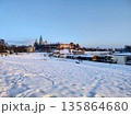 The snow-covered ground leads to the water where boats are. River frosen. Wawel Castle in Krakow, Poland, covered in snow. 135864680
