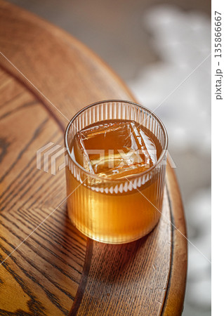 Amber cocktail with ice cube in ribbed glass 135866667