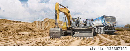 Heavy equipment such as a backhoe loader and dump truck operates on sandy soil under the clouds. A sand quarry at a construction site 135867135