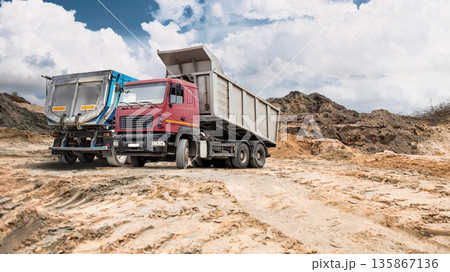 Construction activity is taking place on a large area of dry land with cracked earth. Dirt mounds are visible with trucks and equipment present under a cloudy sky 135867136