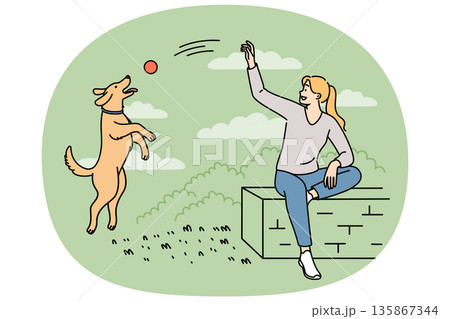 Woman plays with dog in park, tossing ball to bouncing puppy and enjoying perfect sunny weather 135867344