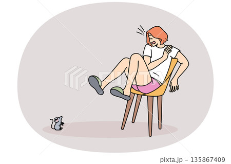 Mouse scares woman jumped onto chair out of fear and experiences musophobia at sight of rodent. 135867409
