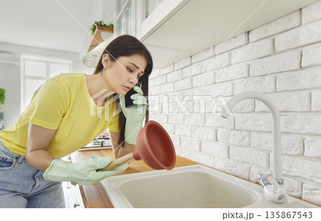 Young girl talking by the phone advising how to unclog a sink drain in the kitchen at home. 135867543