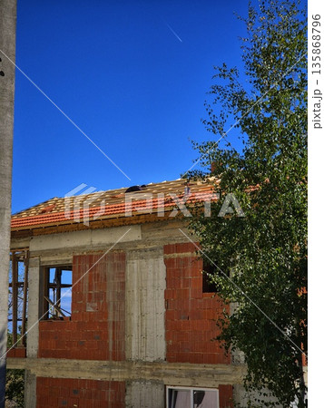A rural house under a blue sky. An unfinished brick building. A house under construction. A house renovation. A rural house under a blue sky. An unfinished brick building. A house under construction. A house renovation. 135868796