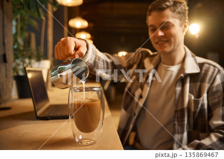 Man pouring milk into double wall glass coffee cup indoors. 135869467