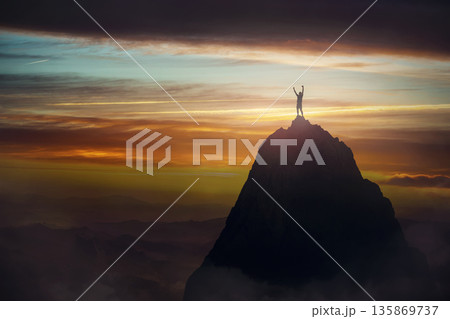 Successful male celebrates victory on a mountain top, raising hands up like a winner. Conceptual and motivational scene inspiring for overcoming challenges. Courageous and victorious person 135869737