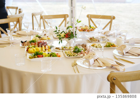 Elegant dining table set for a special event, featuring an array of gourmet dishes, fresh fruits, and decorative floral centerpiece, creating a festive atmosphere Elegant dining table set for a special event, featuring an array of gourmet dishes, fresh fruits, and decorative floral centerpiece, creating a festive atmosphere 135869808