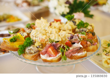 Colorful platter of assorted appetizers featuring various toppings, garnished with fresh herbs, displayed elegantly on a glass serving dish for a festive gathering or event 135869830