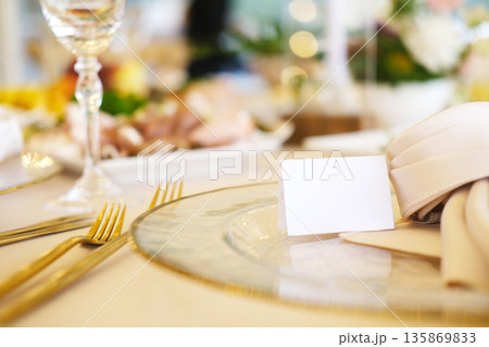 Elegant table setting featuring blank place cards on fine china plates, surrounded by luxurious cutlery and soft floral arrangements, ideal for event design mock up with copy space Elegant table setting featuring blank place cards on fine china plates, surrounded by luxurious cutlery and soft floral arrangements, ideal for event design mock up with copy space 135869833