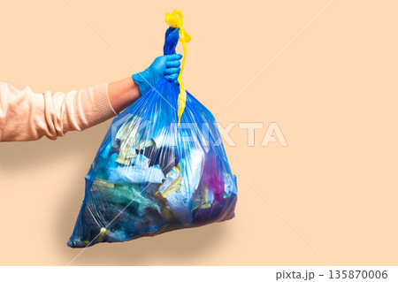Hand holding full garbage bag on beige background isolated. High quality image 135870006