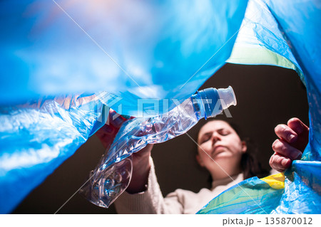 Woman throwing garbage into blue trash bag. Low angle. Look from inside of bag Woman throwing garbage into blue trash bag. Low angle. Look from inside of bag 135870012