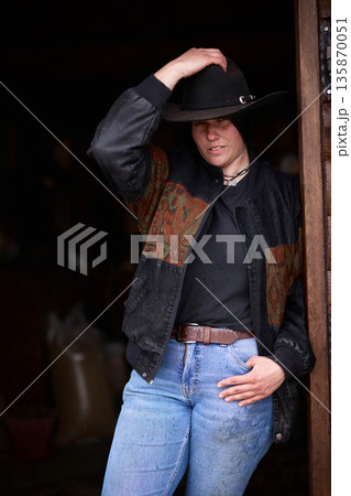 Cowgirl in black hat and denim jeans posing at a rustic ranch doorway, ready for work Cowgirl in black hat and denim jeans posing at a rustic ranch doorway, ready for work 135870051