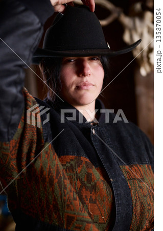 Cowgirl wearing a wide black hat and patterned jacket at a rustic ranch setting Cowgirl wearing a wide black hat and patterned jacket at a rustic ranch setting 135870054