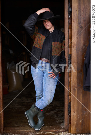 Cowgirl in doorway at rustic ranch wearing hat, jeans, and boots Cowgirl in doorway at rustic ranch wearing hat, jeans, and boots 135870072