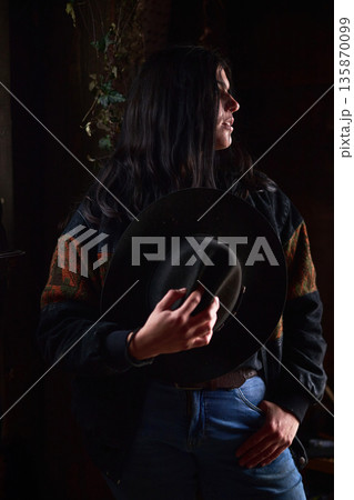 Moody portrait of a woman in a dark hat, denim jeans, and a patterned sweater 135870099