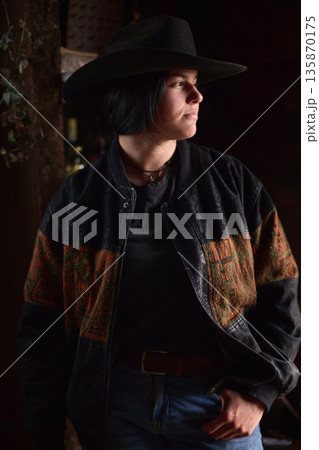 Portrait of a woman in a black hat and denim jacket with Western pattern, moody lighting 135870175