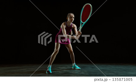 Focused female tennis player ready to receive ball in studio. Focused female tennis player ready to receive ball in studio. 135871005