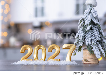 Golden number 2027 on table in background of cozy white kitchen with Christmas tree and Christmas decor with garland lights. Housing, interior, renovation, mortgage, rent in New Year Golden number 2027 on table in background of cozy white kitchen with Christmas tree and Christmas decor with garland lights. Housing, interior, renovation, mortgage, rent in New Year 135872057