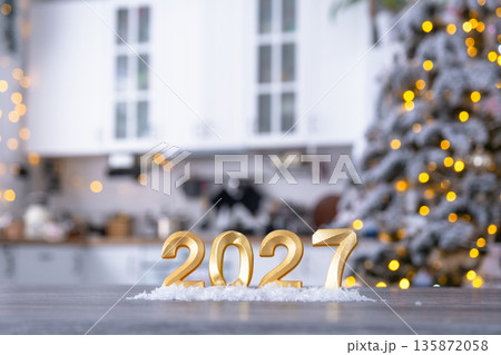 Golden number 2027 on table in background of cozy white kitchen with Christmas tree and Christmas decor with garland lights. Housing, interior, renovation, mortgage, rent in New Year Golden number 2027 on table in background of cozy white kitchen with Christmas tree and Christmas decor with garland lights. Housing, interior, renovation, mortgage, rent in New Year 135872058