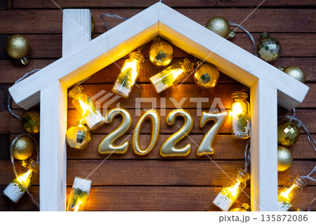 Golden figures number 2027 and tiny home on background of cozy windows of a house with warm light with festive decor of stars,snow and garlands. Greeting card, Happy New Year, cozy home Golden figures number 2027 and tiny home on background of cozy windows of a house with warm light with festive decor of stars,snow and garlands. Greeting card, Happy New Year, cozy home 135872086